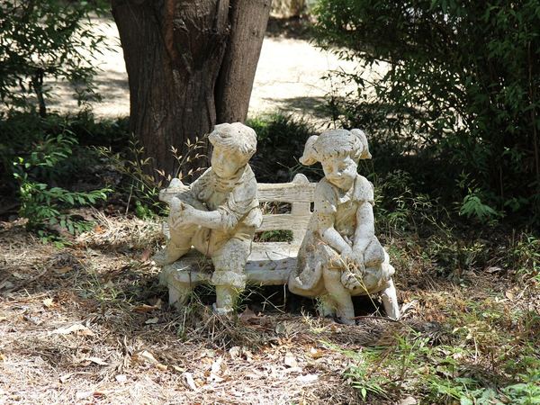 Garden statue of two children on a bench beneath a tree
